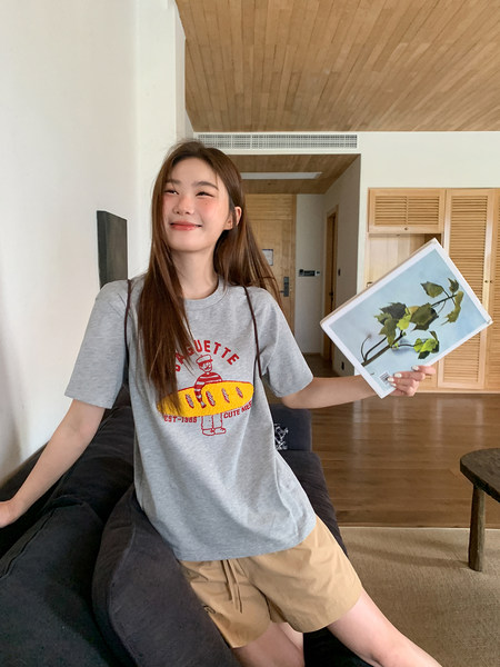 Model wearing a gray graphic T-shirt and beige shorts indoors
