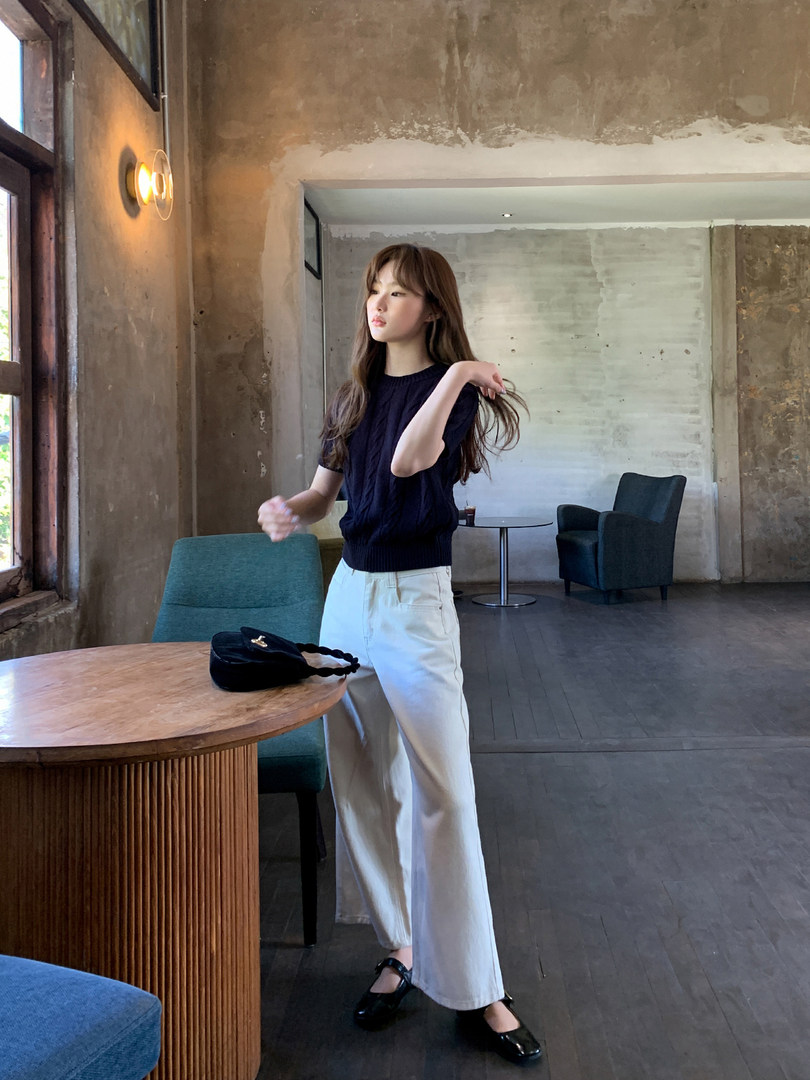 Woman wearing a black knit top with wide-leg white pants and black shoes in a cafe setting