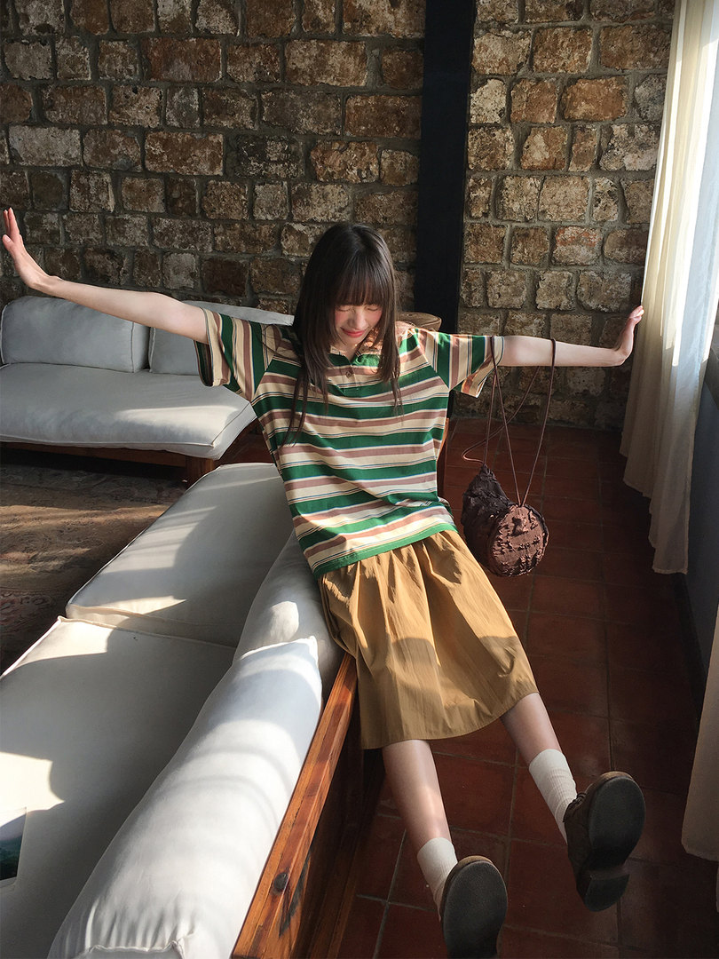 Model wearing a striped short-sleeve polo shirt and brown skirt in a casual indoor setting