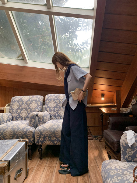 Woman wearing a light gray short-sleeve top with wide navy pants and sandals indoors