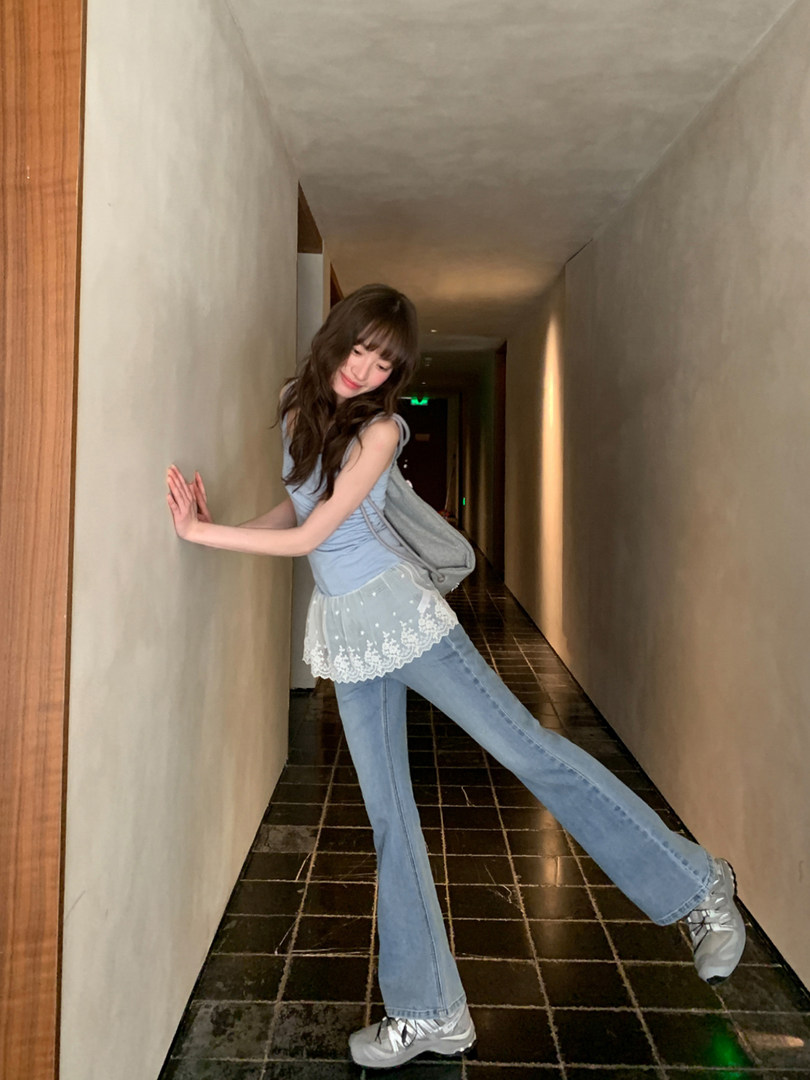Woman wearing a light blue top and flared jeans with a gray backpack in a hallway