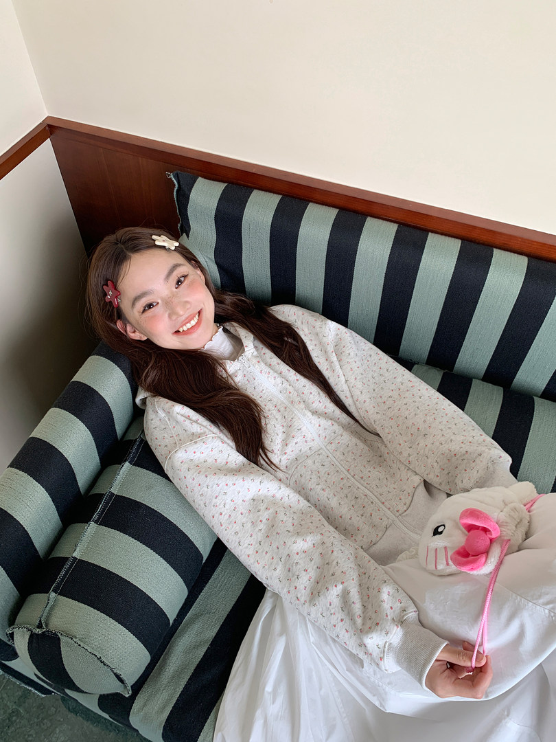 Woman wearing a light floral zip-up hoodie while lounging on a striped couch