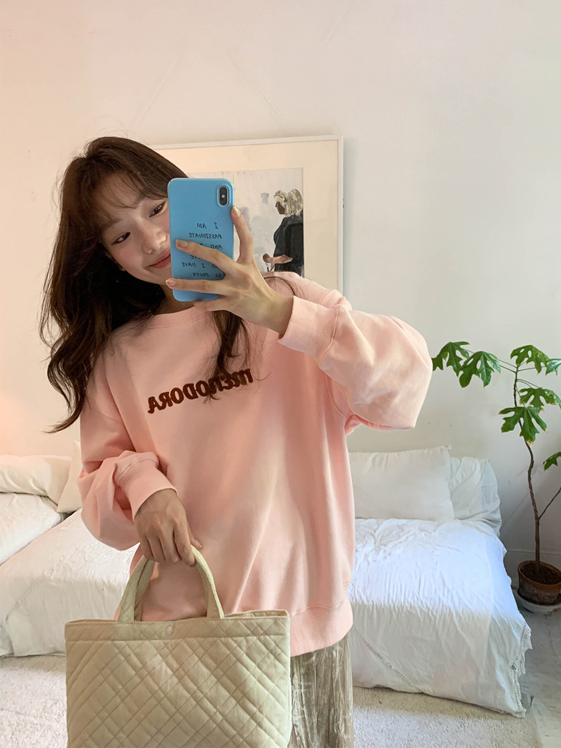 Woman wearing a pink oversized sweatshirt and holding a quilted tote bag