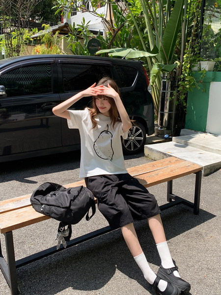 Model wearing a white graphic T-shirt, black shorts, and black backpack outdoors