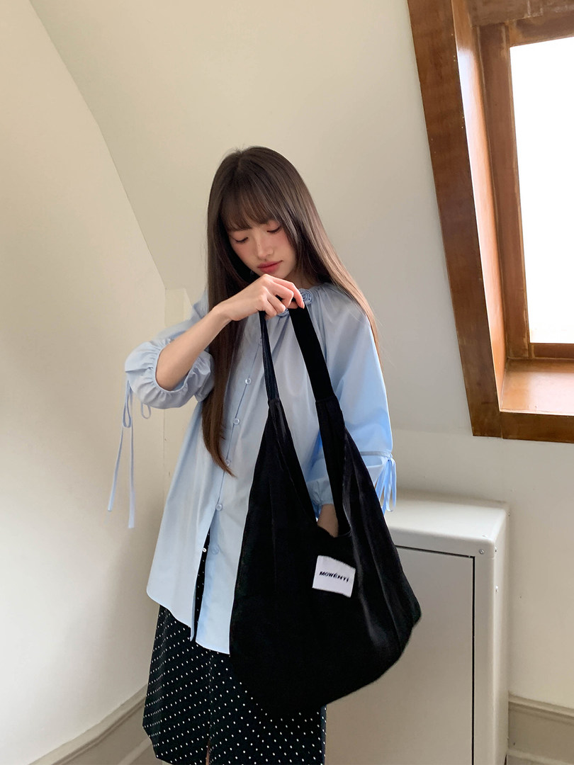 Black tote bag worn by a woman indoors