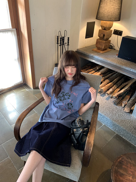 Model wearing a blue graphic T-shirt with a dark denim skirt and black bag
