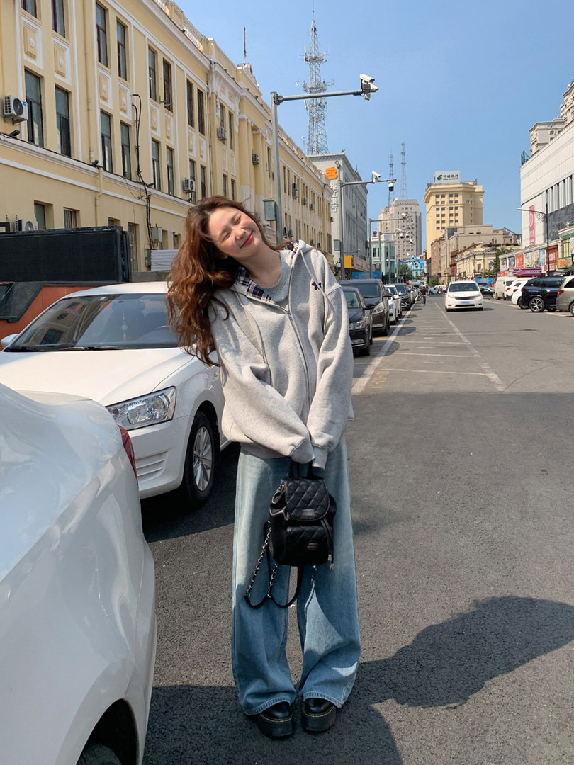 Woman wearing a gray oversized hoodie with wide-leg jeans and a black mini backpack on a city street
