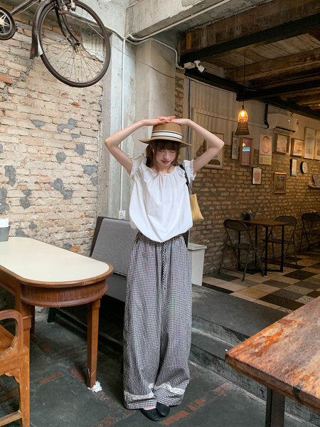 Woman wearing a white sleeveless top and gingham wide-leg pants with a straw hat
