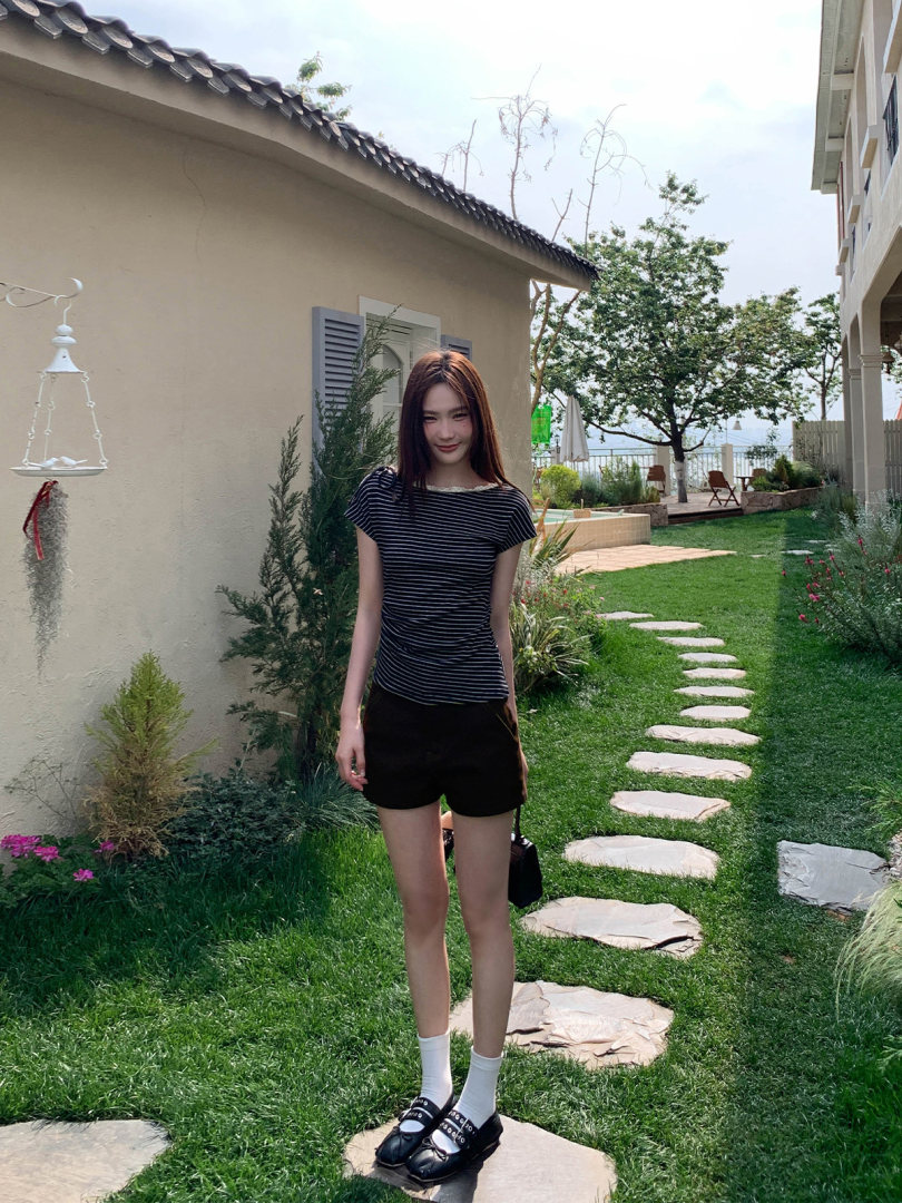 Woman wearing a black striped top with black shorts and loafers outdoors