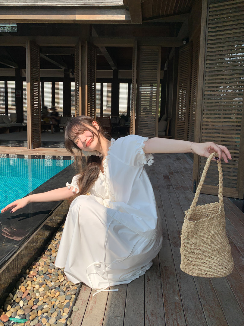 Woman wearing a white dress and holding a woven straw tote by a pool