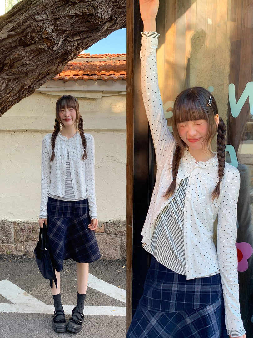 Model wearing a white polka dot cardigan and layered top with a navy plaid skirt