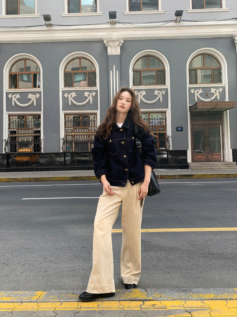Model wearing a dark jacket and beige wide-leg pants on a city street