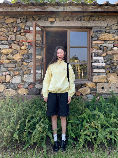 Model wearing a light yellow zip-up jacket with dark shorts and black shoes outdoors