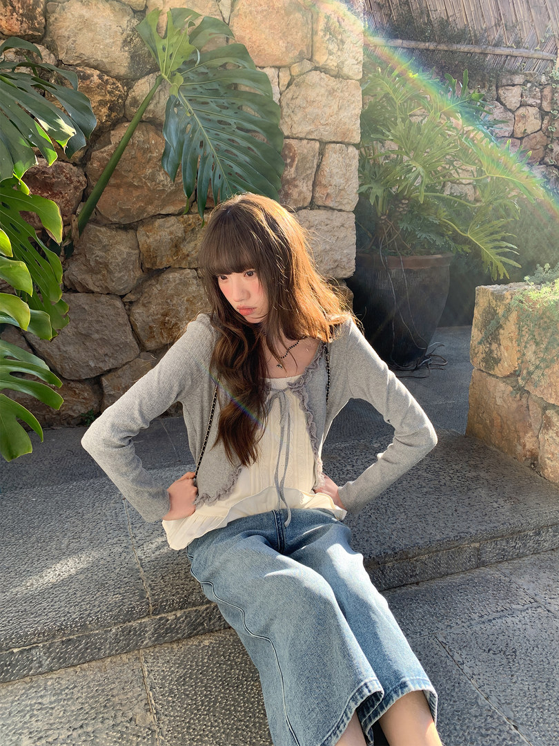 Young woman wearing a gray cardigan, cream top, and light blue jeans outdoors