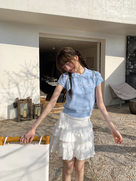 Woman wearing a light blue knit polo top and white tiered lace skirt outdoors