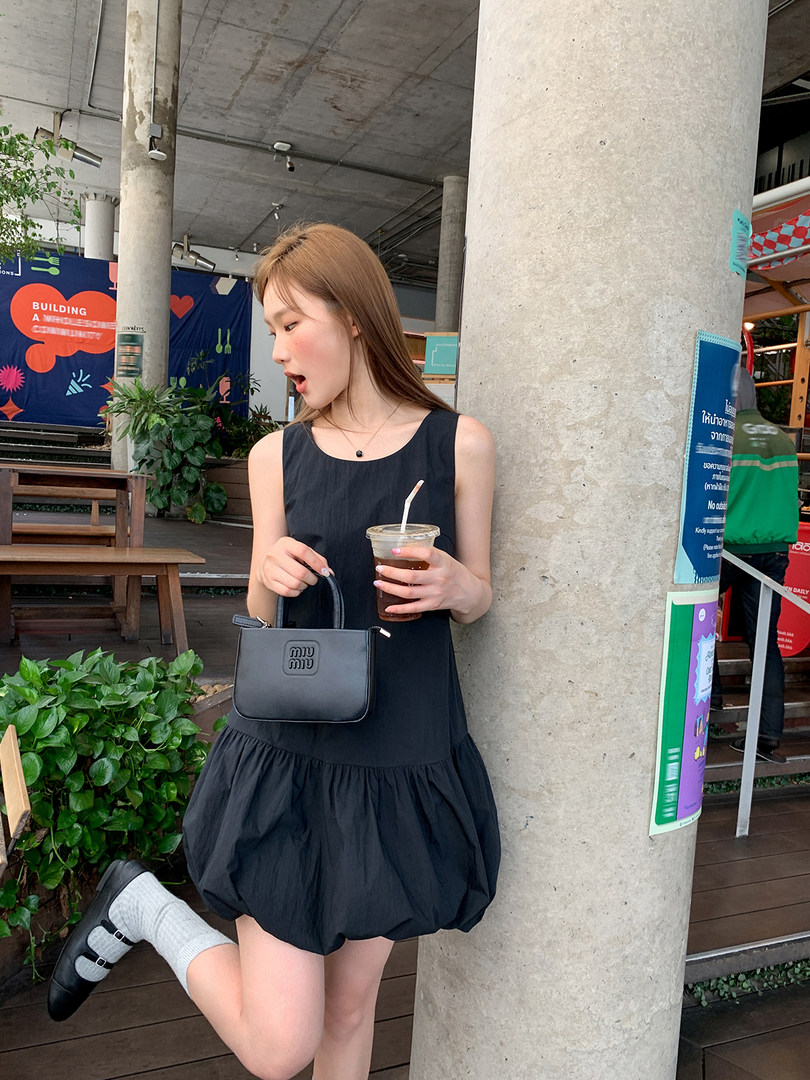 Black sleeveless bubble-hem dress worn by a woman with a small black handbag