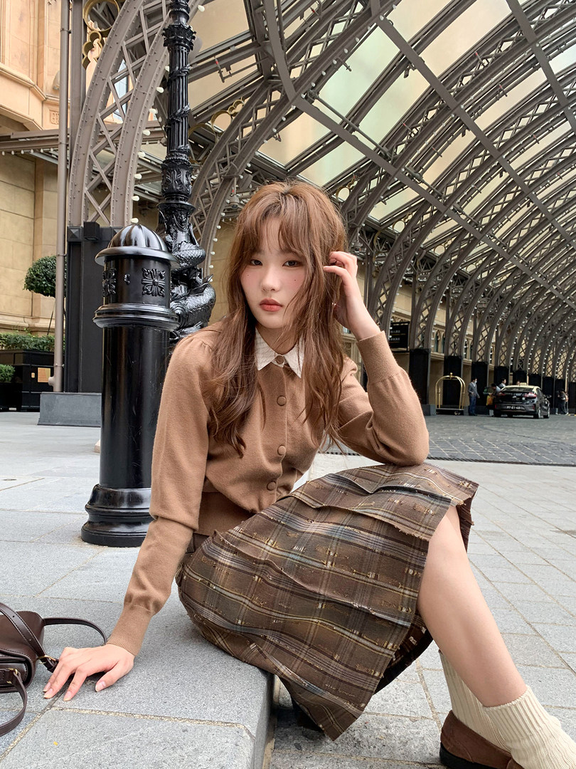 Woman wearing a brown cardigan and plaid skirt outdoors