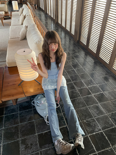 Young woman wearing a light blue camisole, lace layer, jeans, and sneakers indoors