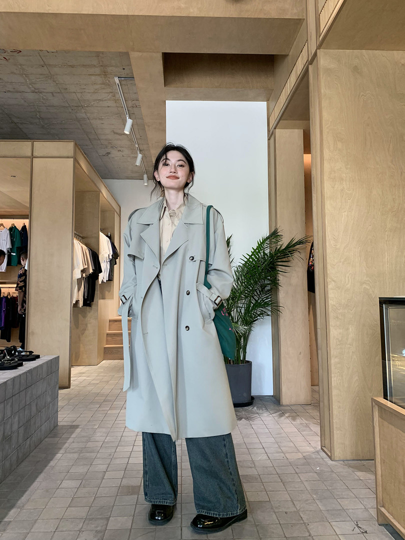 Woman wearing a light beige trench coat over casual jeans in a store