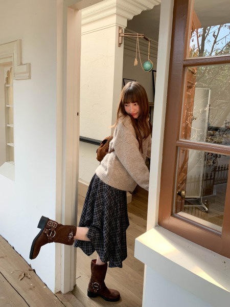 Woman wearing a cozy sweater, plaid skirt, and brown boots