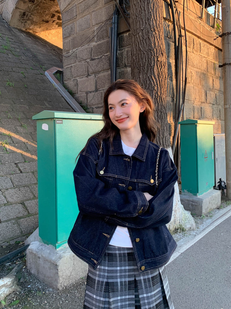 Woman wearing a dark denim jacket with a plaid skirt outdoors