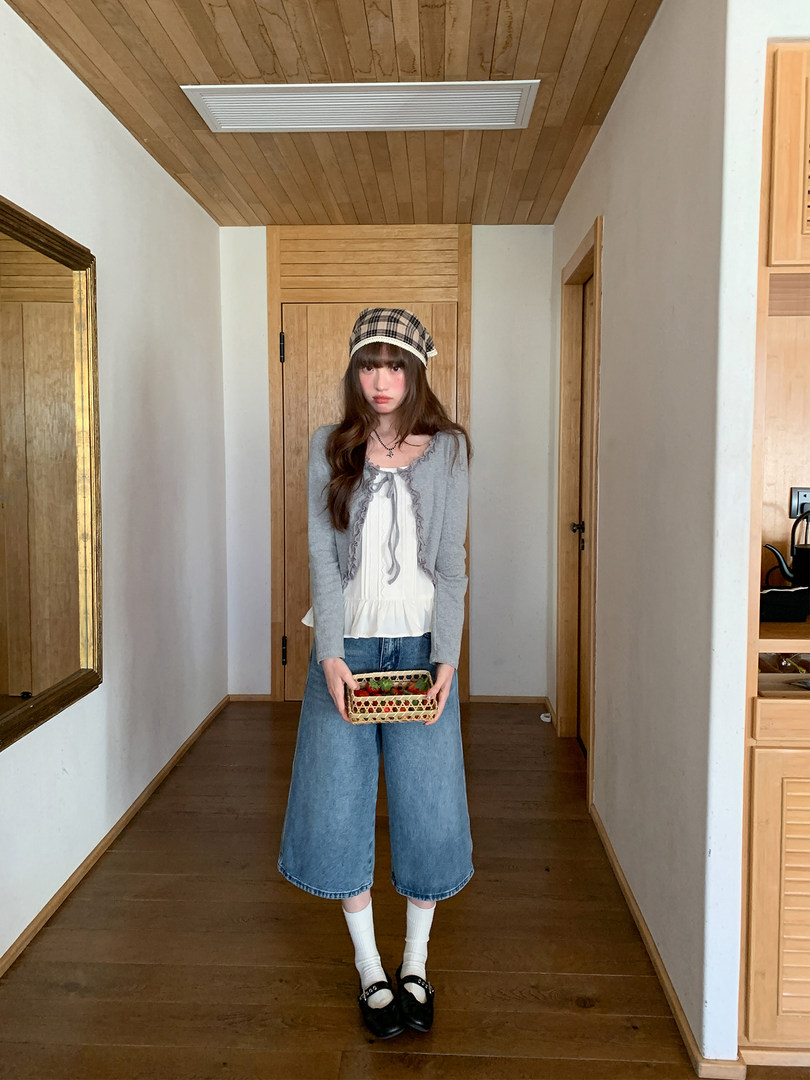 Young woman modeling a casual outfit with a plaid hat, gray cardigan, white top, wide-leg jeans, and black shoes