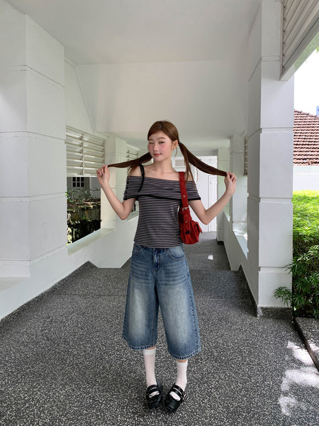 Model wearing a striped off-shoulder top with wide-leg denim pants and a red shoulder bag