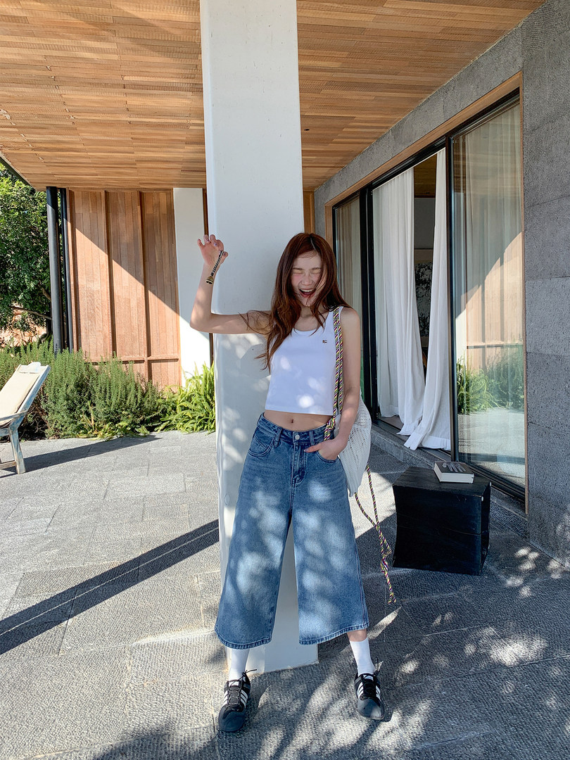 Woman wearing a white tank top with wide-leg blue jeans and sneakers outdoors