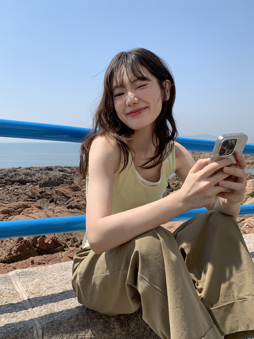 Woman wearing a light yellow tank top and loose olive pants outdoors by the sea