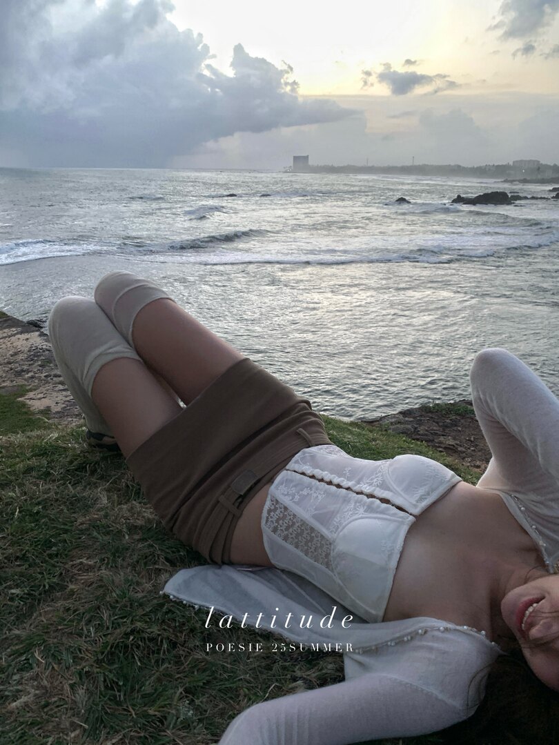 Model wearing a white lace top and brown wrap bottom by the seaside