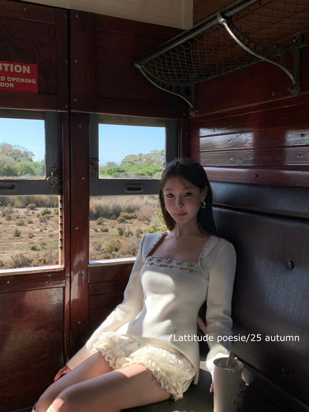 Woman wearing a white long-sleeve dress with lace trim while seated in a train car