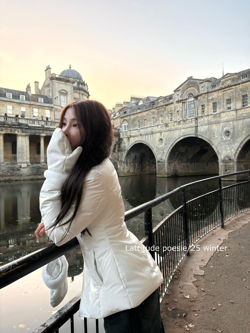 Woman wearing a white winter puffer coat outdoors by a historic waterfront