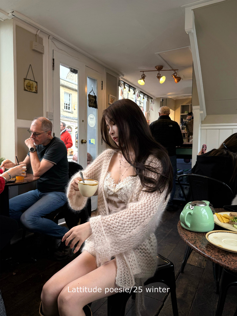 Woman wearing a fluffy light pink cardigan and lace lingerie while seated in a cafe holding a cup