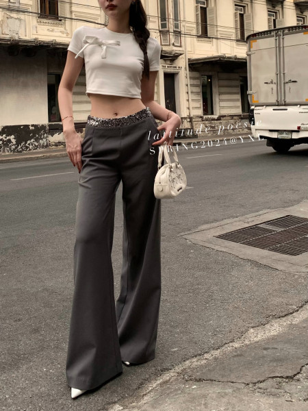 Model wearing a white cropped bow top with dark wide-leg trousers and a small handbag