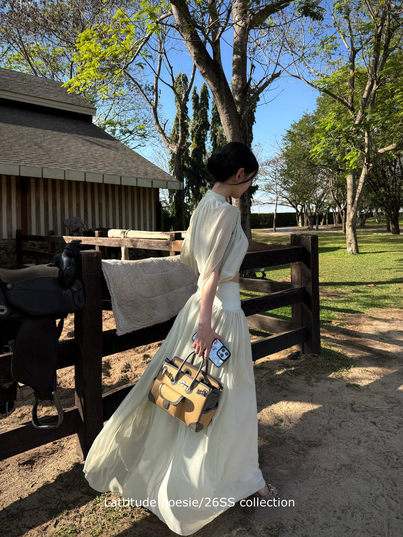Woman wearing a flowing cream dress outdoors while holding a handbag