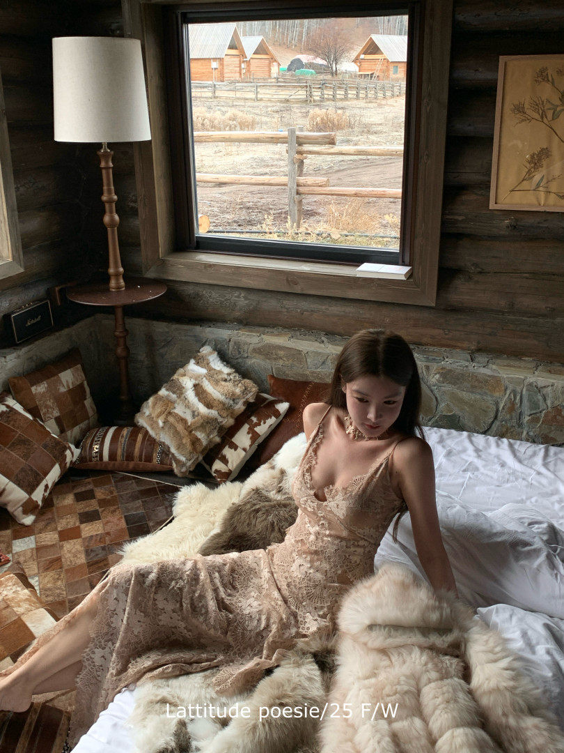 Model wearing a beige lace dress in a rustic bedroom setting