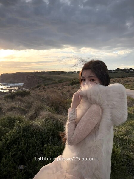 Woman wearing a sheer lace dress with a fluffy white wrap outdoors at sunset