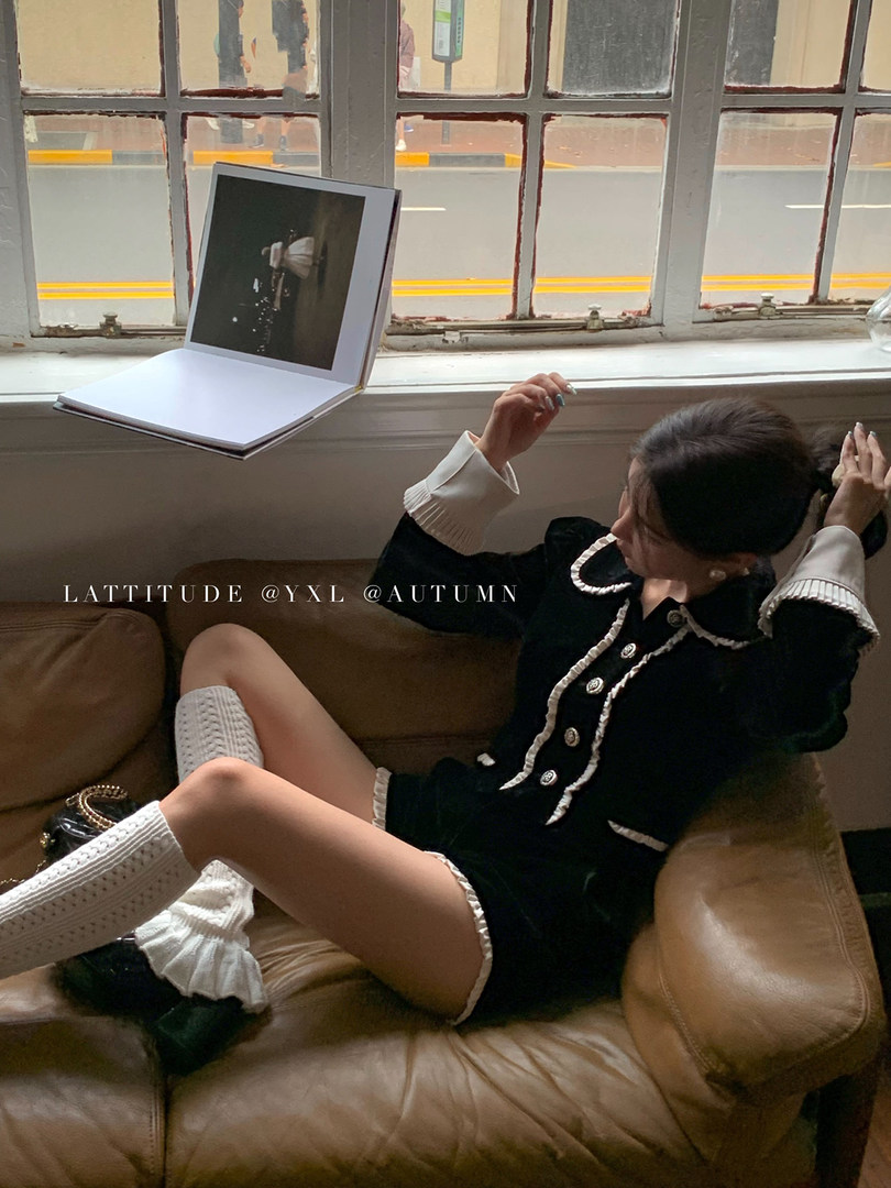 Model wearing a black and white autumn-inspired outfit while lounging on a sofa