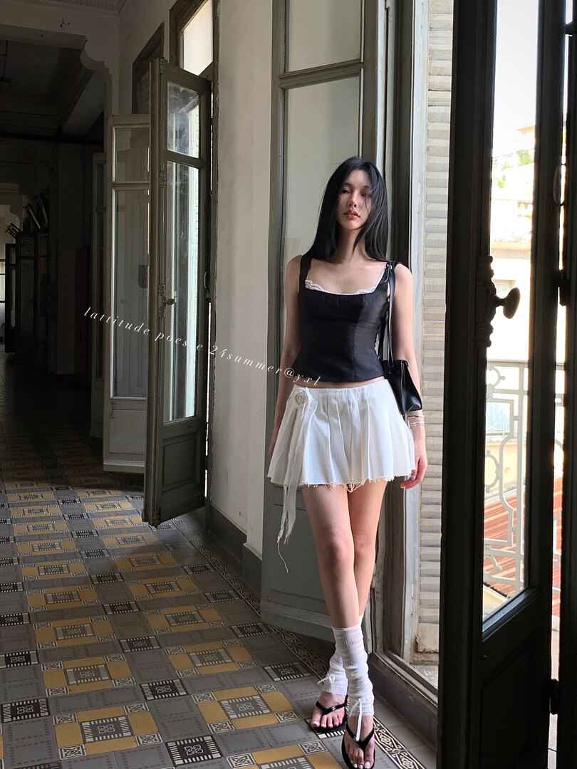 Model wearing a black sleeveless top with a white pleated mini skirt and sandals