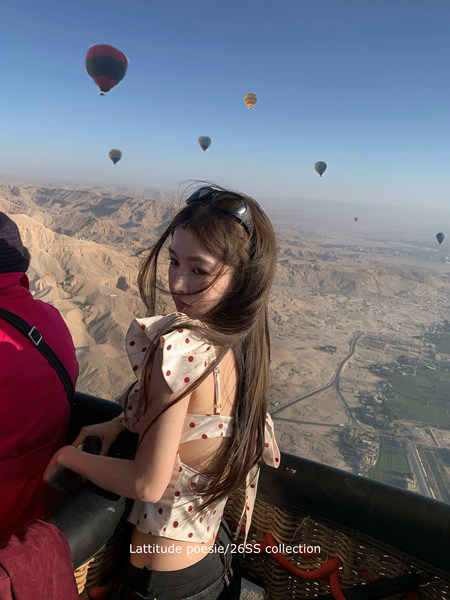 Woman wearing a white polka dot crop top during a hot air balloon ride over a desert landscape