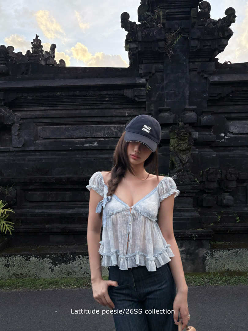 Model wearing a light blue ruffled camisole top with jeans and a cap
