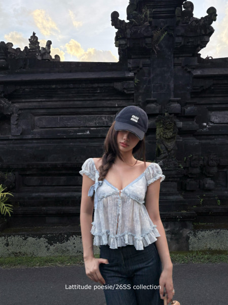 Model wearing a light blue ruffled camisole top with jeans and a cap