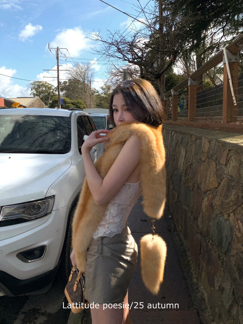Woman wearing a golden fur stole over a lace top and gray skirt outdoors