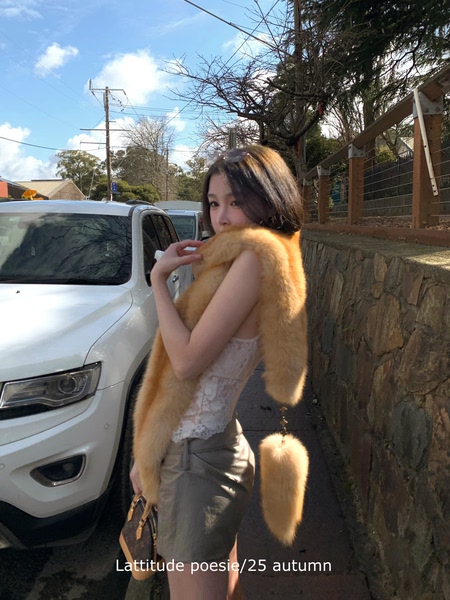 Woman wearing a golden fur stole over a lace top and gray skirt outdoors