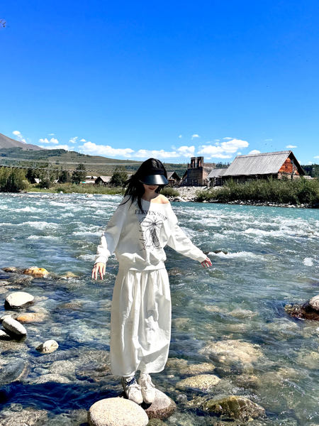 Woman wearing a white graphic sweatshirt and long skirt by a river