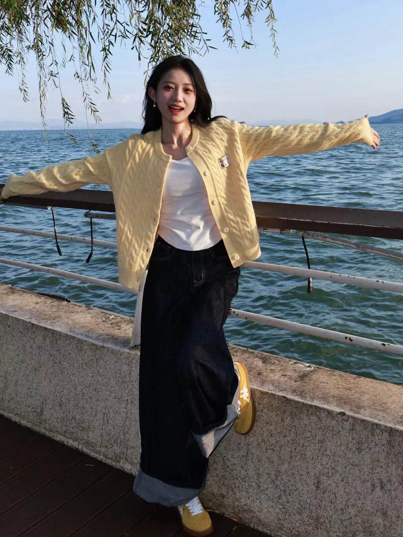 Woman wearing a pale yellow cable-knit cardigan over a white top and black skirt by the waterfront