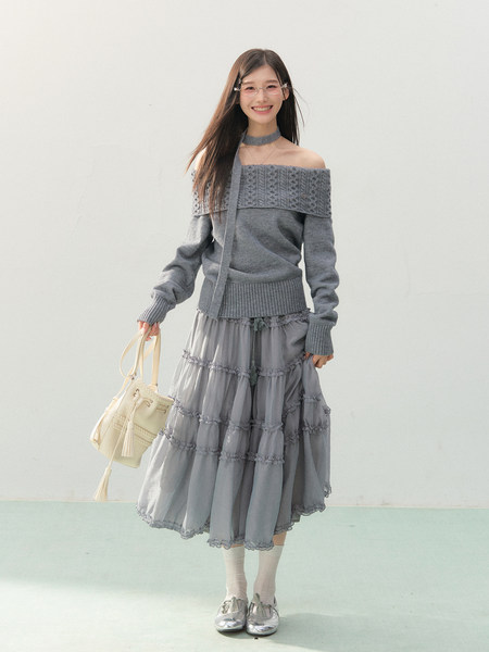 Woman modeling a gray off-shoulder knit top with a layered skirt and cream handbag