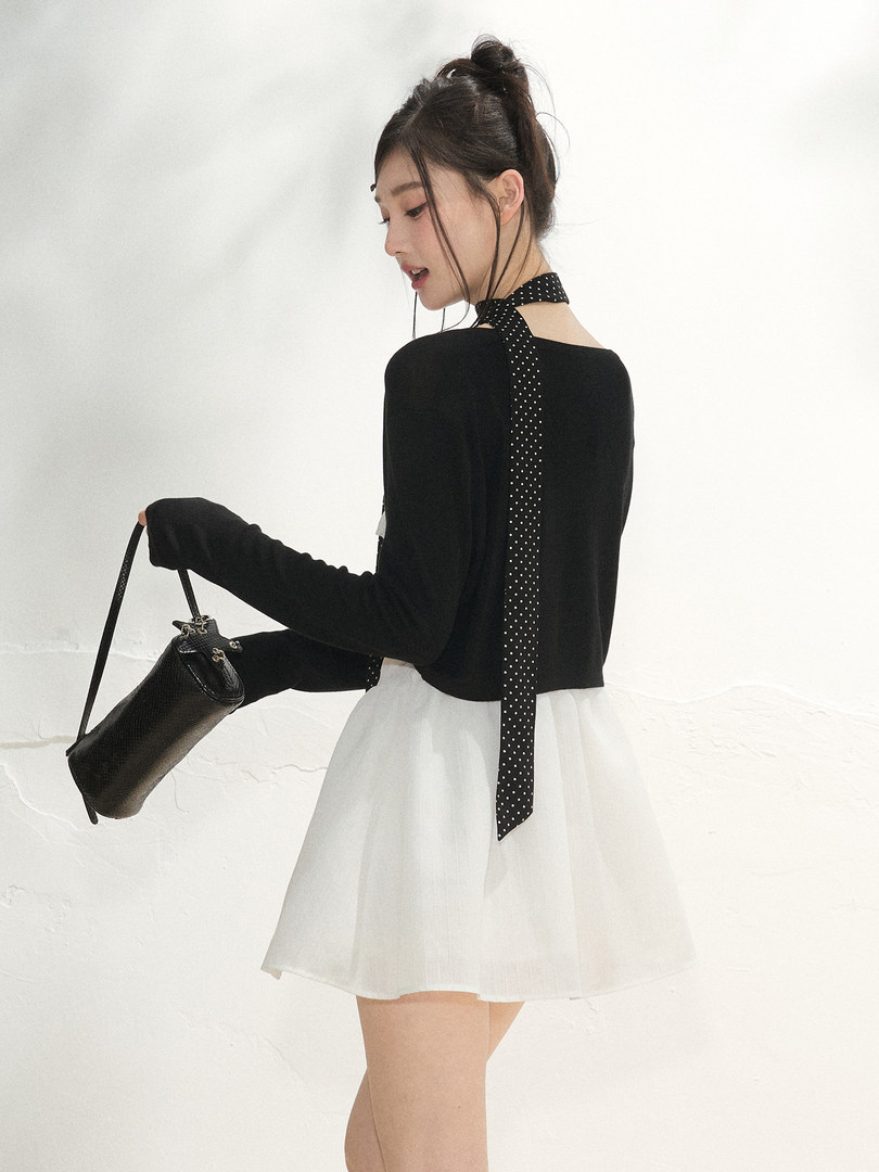 Model wearing a black top and white skirt while holding a black handbag