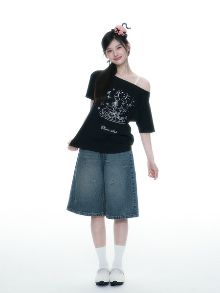 Model wearing a black off-shoulder graphic top with a denim skirt