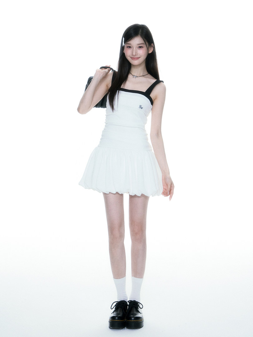 Model wearing a white sleeveless mini dress with black straps and black platform shoes